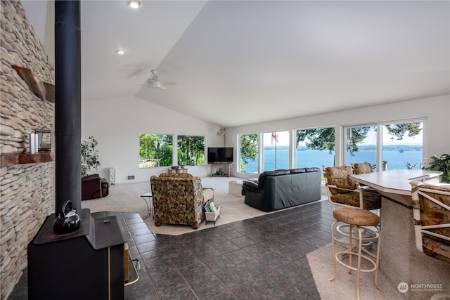 tiled living room featuring lofted ceiling, ceiling fan, a water view, and a wood stove