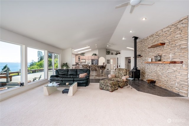 carpeted living room featuring a wood stove, ceiling fan, vaulted ceiling, and a water view