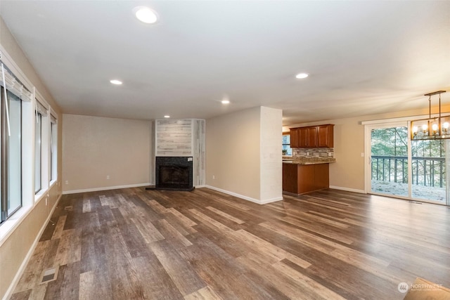 unfurnished living room featuring dark wood-type flooring, a tile fireplace, and an inviting chandelier