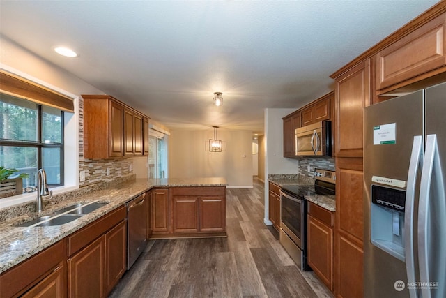 kitchen with kitchen peninsula, appliances with stainless steel finishes, sink, decorative light fixtures, and dark hardwood / wood-style floors