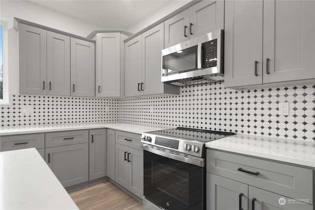 kitchen featuring gray cabinets, stainless steel appliances, decorative backsplash, and light hardwood / wood-style flooring