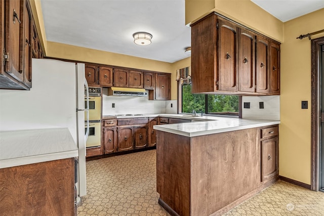 kitchen with double oven, light tile floors, backsplash, extractor fan, and kitchen peninsula