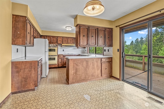 kitchen with white appliances, backsplash, kitchen peninsula, extractor fan, and light tile floors