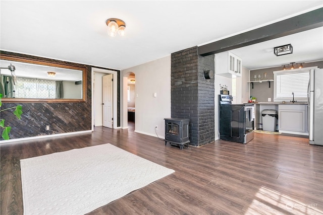 living room featuring beamed ceiling, a wood stove, dark wood-type flooring, and sink