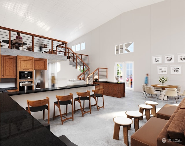 kitchen with brown cabinetry, light colored carpet, a kitchen breakfast bar, high vaulted ceiling, and stainless steel refrigerator with ice dispenser