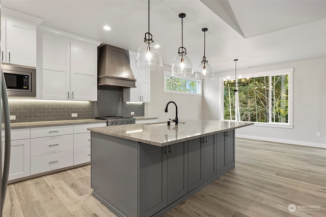 kitchen with hanging light fixtures, white cabinetry, an island with sink, and premium range hood