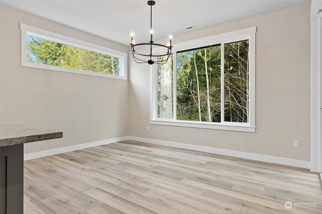 unfurnished dining area with an inviting chandelier and light hardwood / wood-style flooring