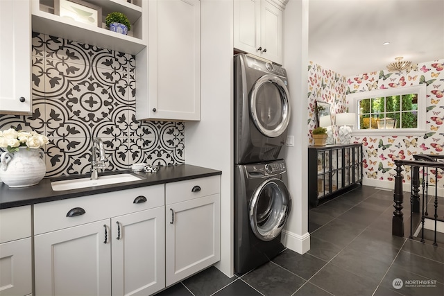 laundry area featuring stacked washer and dryer, dark tile flooring, and sink