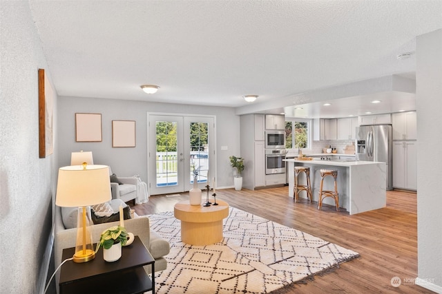 living room featuring french doors, a textured ceiling, and light hardwood / wood-style floors