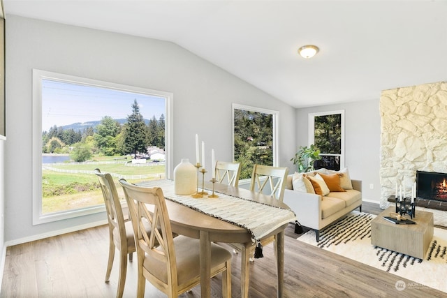 dining space featuring a stone fireplace, wood-type flooring, and vaulted ceiling