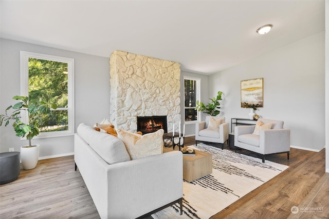 living room featuring a stone fireplace, lofted ceiling, and hardwood / wood-style flooring