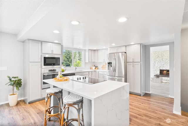 kitchen with a kitchen bar, appliances with stainless steel finishes, sink, light hardwood / wood-style flooring, and a center island