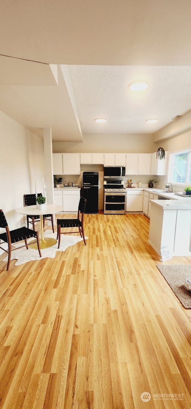 kitchen with stainless steel range, a textured ceiling, sink, white cabinets, and light hardwood / wood-style floors