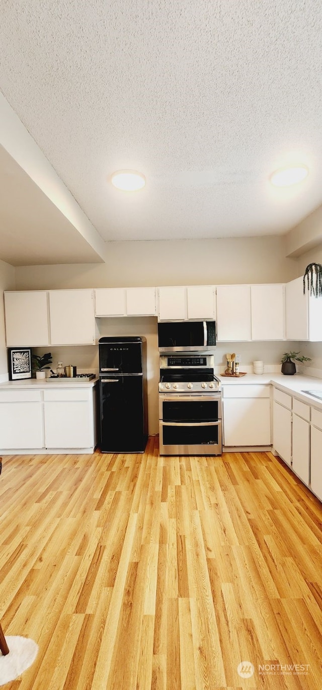 kitchen featuring appliances with stainless steel finishes, light wood-type flooring, a textured ceiling, and white cabinetry