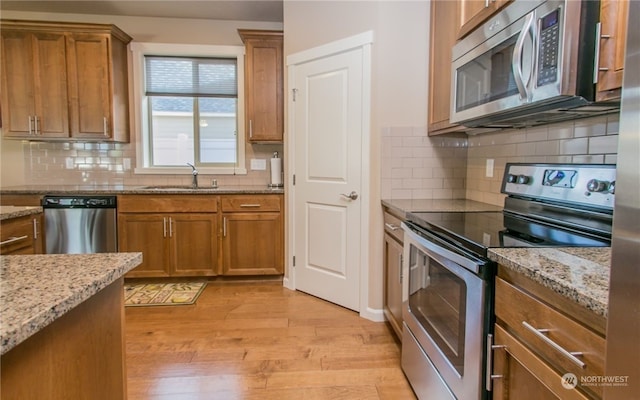 kitchen with sink, light wood-type flooring, appliances with stainless steel finishes, light stone countertops, and decorative backsplash