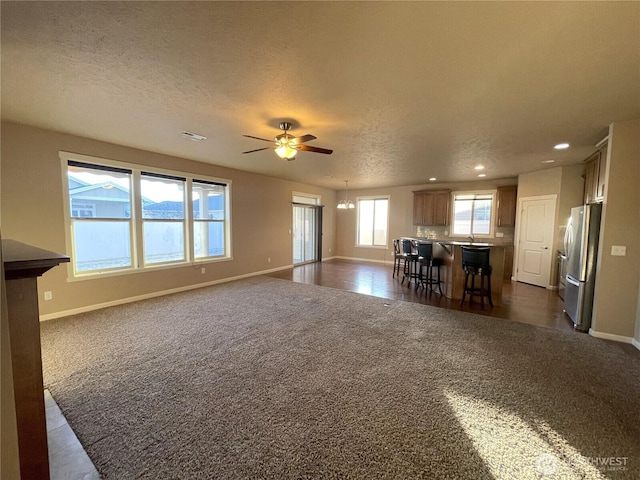 unfurnished living room with ceiling fan with notable chandelier, dark carpet, and a textured ceiling