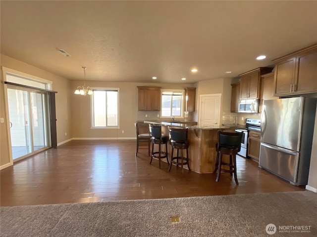 kitchen featuring a breakfast bar area, stainless steel appliances, light stone countertops, a kitchen island, and decorative light fixtures