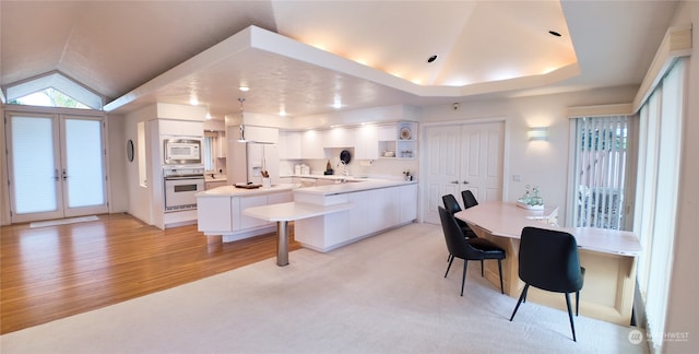 kitchen featuring white appliances, white cabinets, a kitchen breakfast bar, vaulted ceiling, and kitchen peninsula