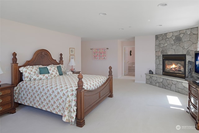 carpeted bedroom featuring a stone fireplace and ensuite bath