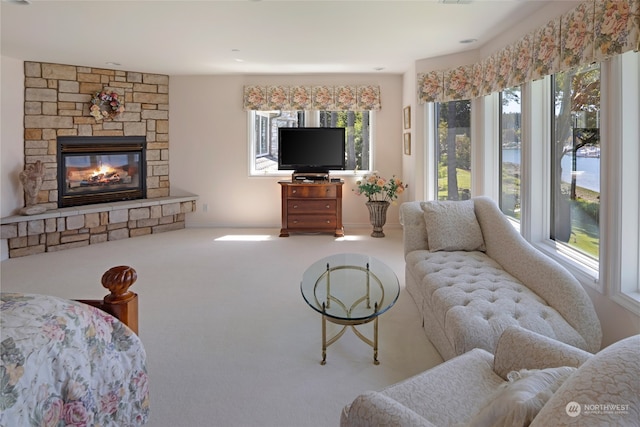 living room featuring a stone fireplace, plenty of natural light, and carpet floors