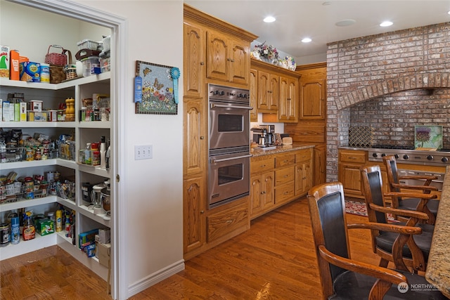 kitchen with light stone countertops, double oven, and hardwood / wood-style floors