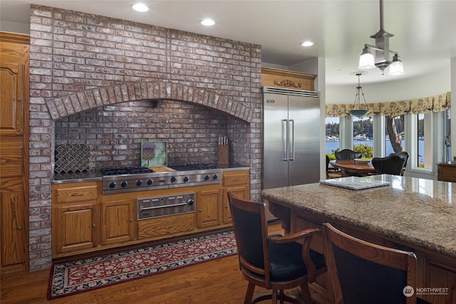 kitchen with stainless steel appliances, hanging light fixtures, hardwood / wood-style flooring, a kitchen bar, and dark stone countertops