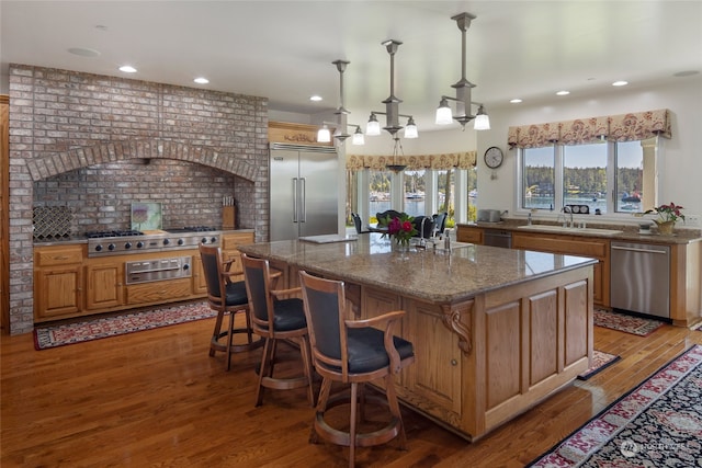 kitchen with a center island, hanging light fixtures, stainless steel appliances, wood-type flooring, and sink