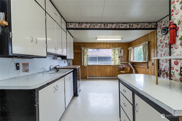 kitchen with white cabinets, baseboard heating, wooden walls, and sink