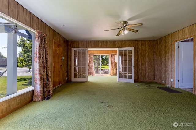 carpeted spare room with wood walls, french doors, and ceiling fan