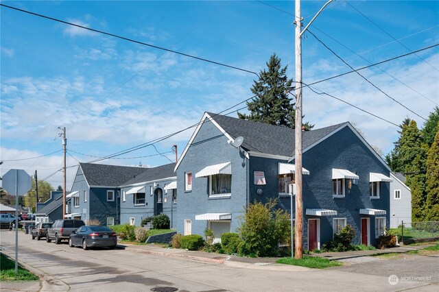 view of front facade with roof with shingles, a residential view, and brick siding