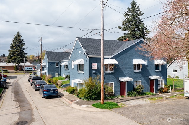 view of property featuring roof with shingles, a residential view, and brick siding