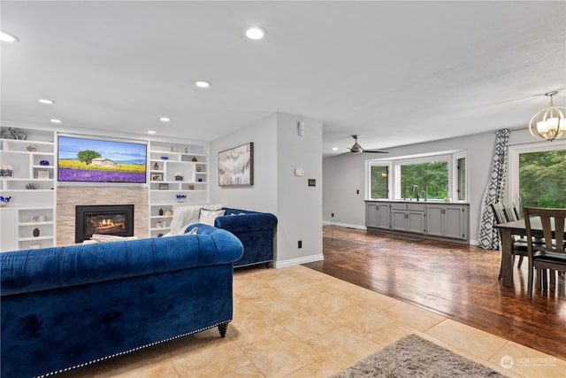 living room featuring light tile floors, a fireplace, sink, ceiling fan with notable chandelier, and built in features