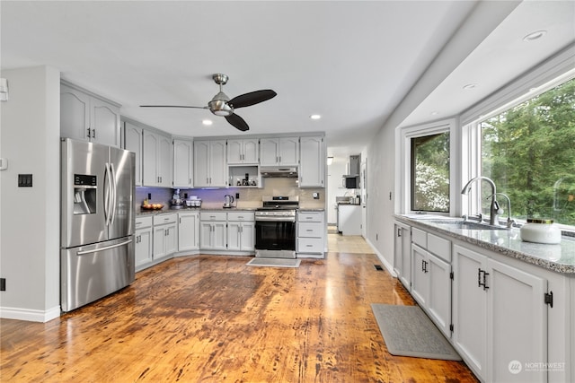 kitchen with hardwood / wood-style floors, stainless steel appliances, sink, light stone counters, and ceiling fan