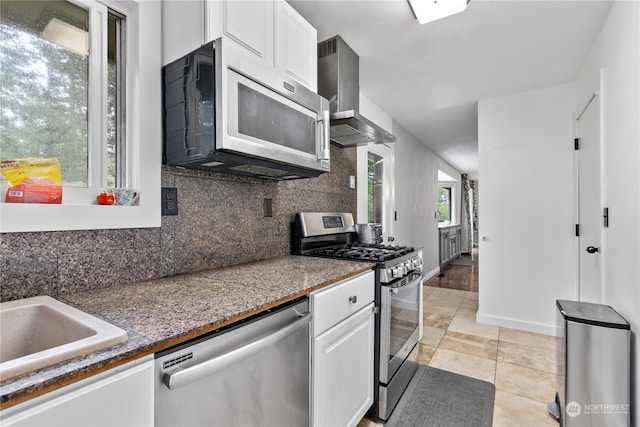 kitchen featuring appliances with stainless steel finishes, backsplash, light tile flooring, wall chimney range hood, and white cabinets