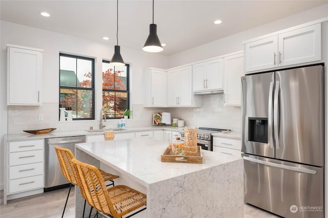 kitchen with stainless steel appliances, light stone counters, a kitchen island, sink, and white cabinetry