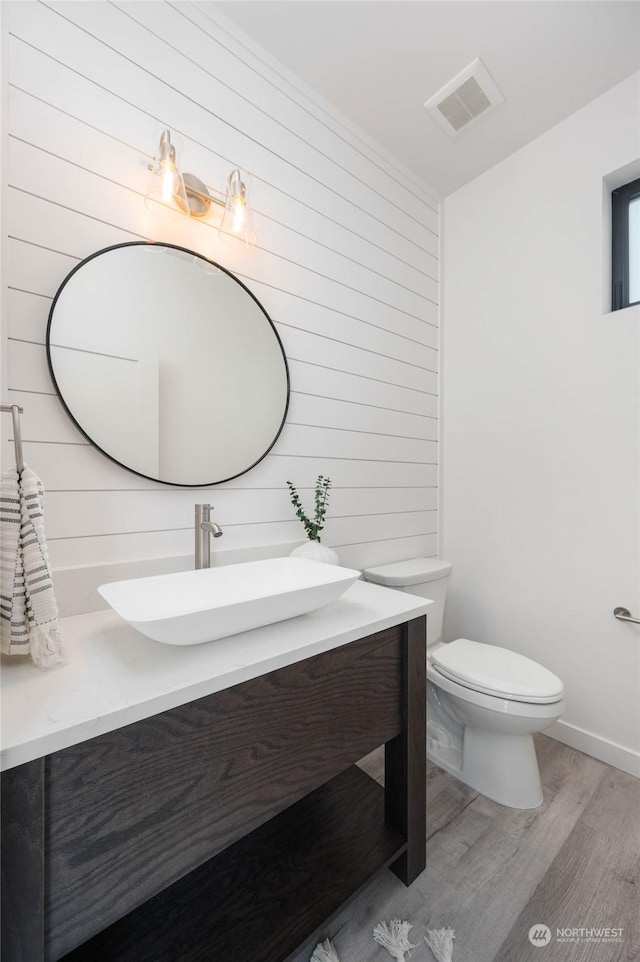 bathroom with toilet, vanity, hardwood / wood-style floors, and wooden walls