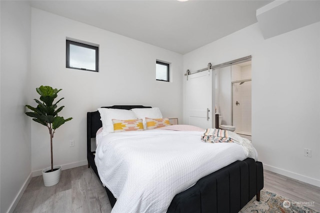 bedroom with connected bathroom, light hardwood / wood-style floors, and a barn door