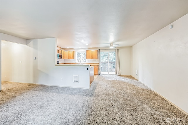 unfurnished living room featuring light colored carpet, sink, and ceiling fan