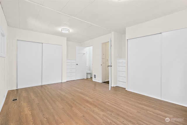 unfurnished bedroom featuring light hardwood / wood-style flooring, ensuite bath, and two closets