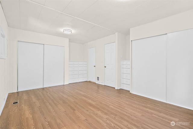 unfurnished bedroom with light hardwood / wood-style flooring and two closets