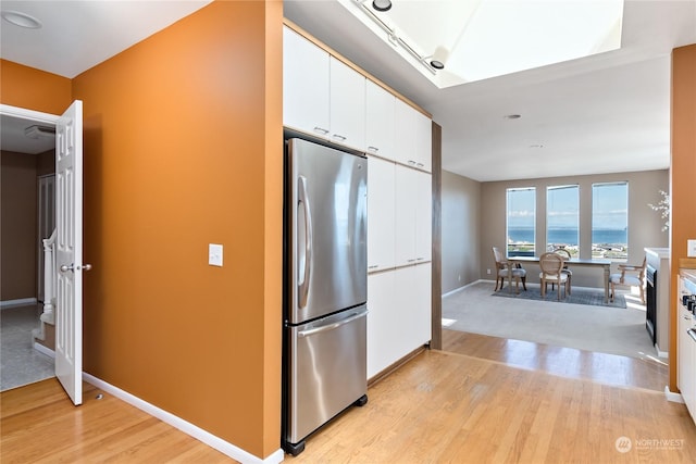 kitchen with white cabinets, stainless steel fridge, a water view, and light hardwood / wood-style flooring