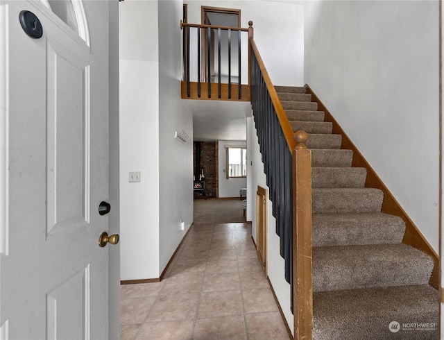 staircase with tile patterned floors, a wood stove, and a towering ceiling