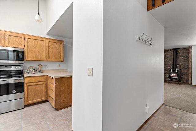 kitchen with light carpet, appliances with stainless steel finishes, a wood stove, and pendant lighting