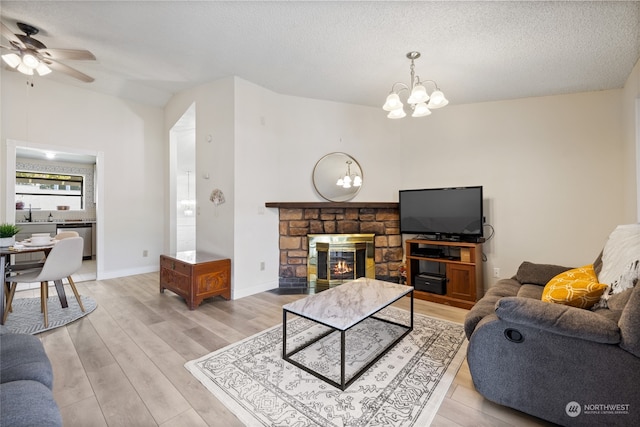 living room with wood-type flooring, ceiling fan with notable chandelier, a fireplace, and a textured ceiling