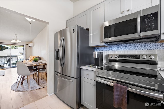 kitchen featuring gray cabinetry, backsplash, an inviting chandelier, appliances with stainless steel finishes, and light hardwood / wood-style floors