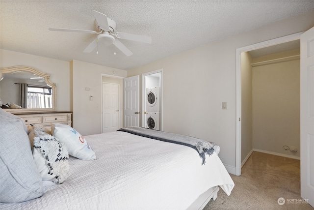 bedroom featuring light colored carpet, ensuite bath, ceiling fan, a textured ceiling, and stacked washing maching and dryer