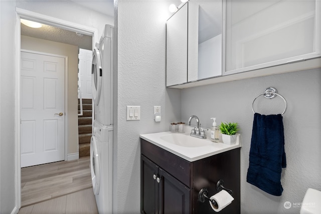 bathroom with hardwood / wood-style flooring, stacked washing maching and dryer, a textured ceiling, and large vanity