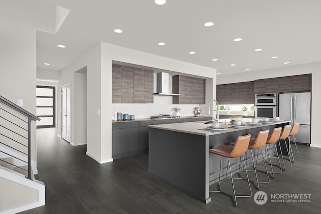 kitchen with appliances with stainless steel finishes, wall chimney range hood, a kitchen island with sink, and dark wood-type flooring