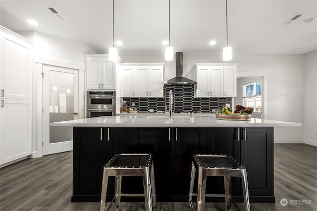 kitchen featuring a large island with sink, white cabinetry, wall chimney exhaust hood, and pendant lighting