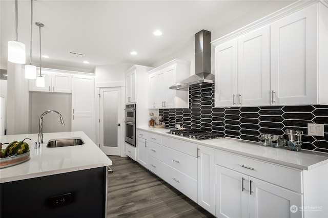 kitchen featuring appliances with stainless steel finishes, sink, wall chimney range hood, dark hardwood / wood-style floors, and hanging light fixtures